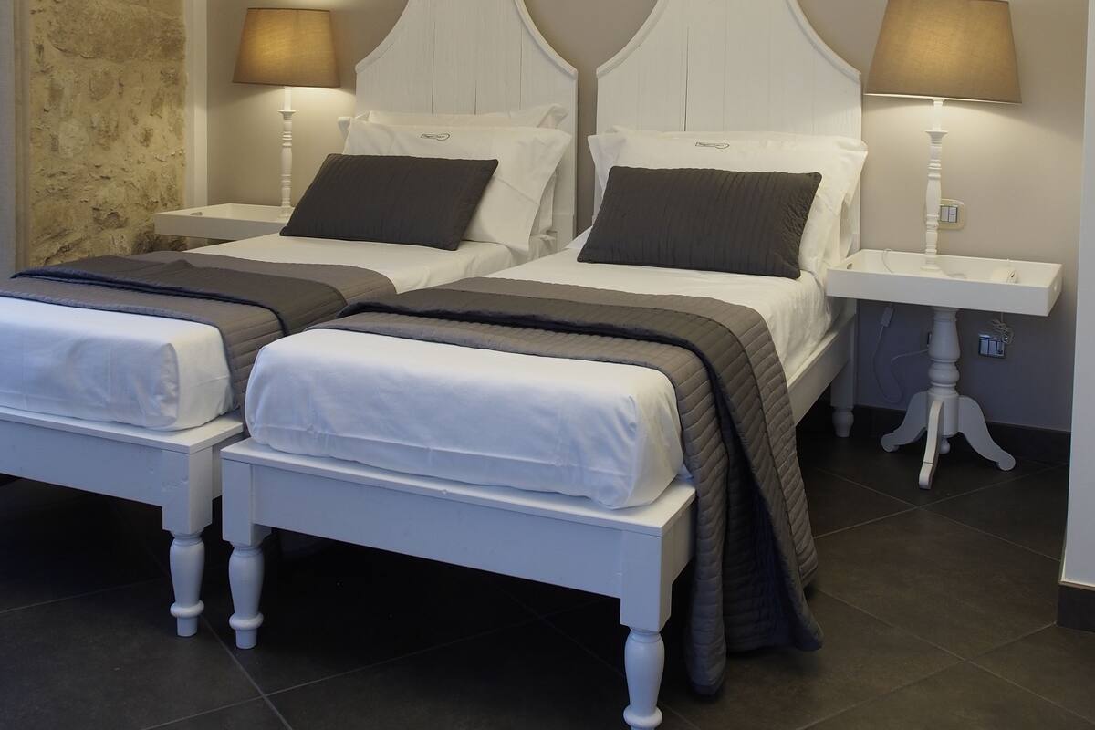 A double bed with two bedside tables, each with a lamp. The room has a stone wall on one side and a plain wall on the other.