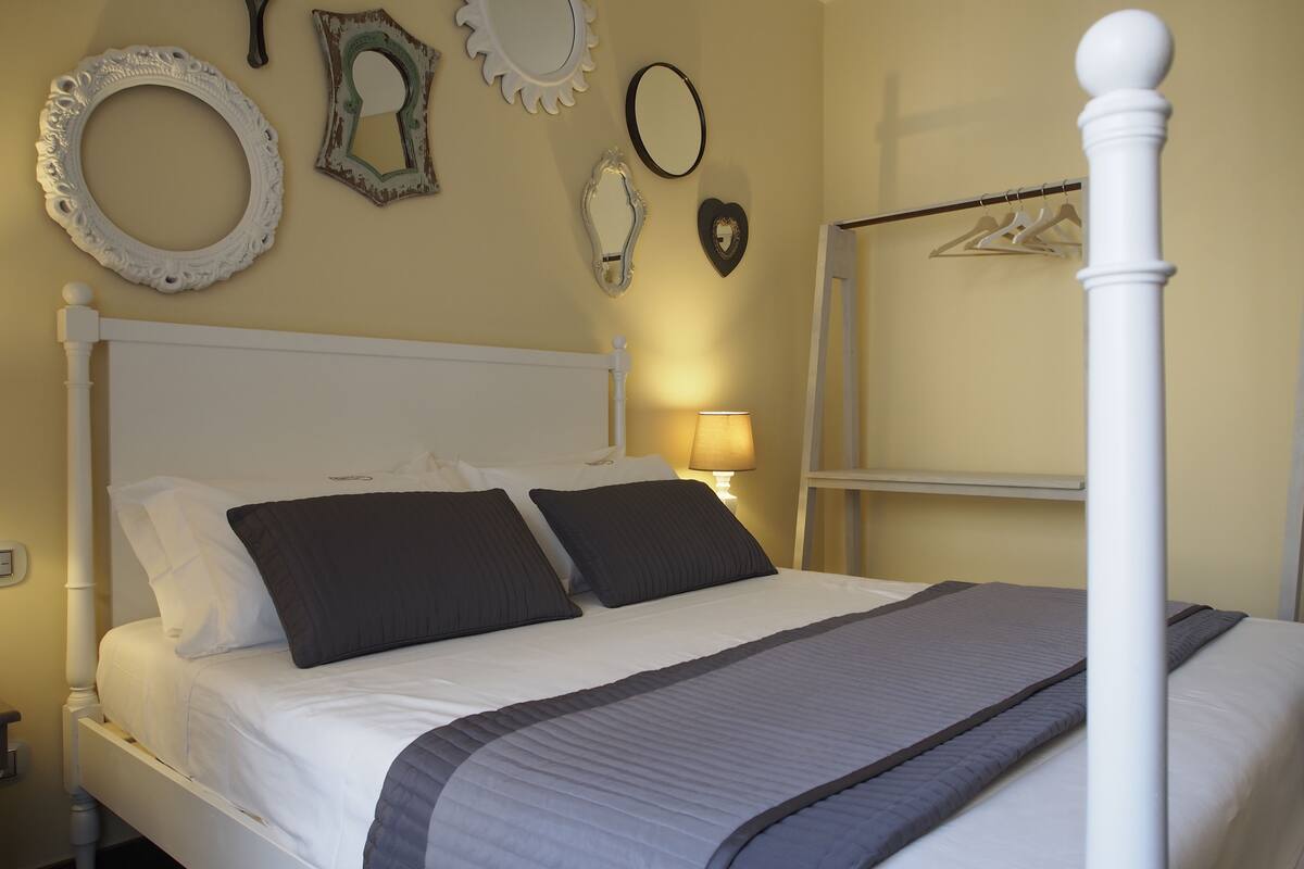 A neatly made bed with white and dark gray bedding, a white headboard, and a bedside table with a lamp.