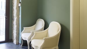 A room with a green wall, a chandelier, two white chairs, and a door. - Terrazzani Suite (Comiso)
