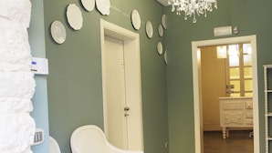 A hallway with a white door, a white chair, a chandelier, and a vanity with a mirror. - Terrazzani Suite (Comiso)