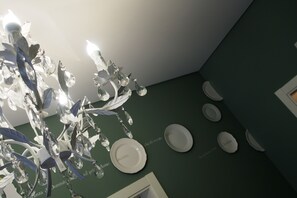 A chandelier with crystal decorations and a green wall with white plates. - Terrazzani Suite (Comiso)