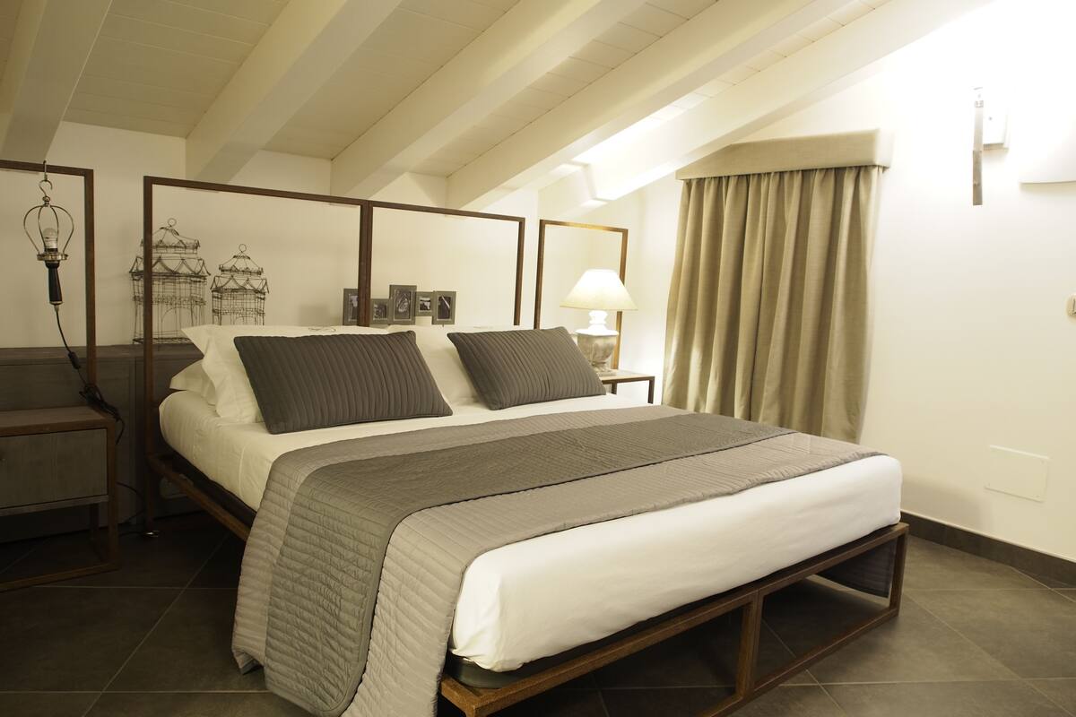 A neatly arranged bedroom with a large bed, a bedside table, a lamp, and a wall-mounted light fixture.