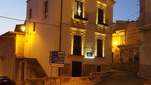 A two-story building with a sign indicating directions to Catania, Ragusa, Croce Camerina, and Vittoria. - Terrazzani Suite (Comiso)