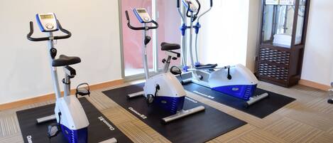 Three stationary bikes on black mats in a room with a wooden floor.