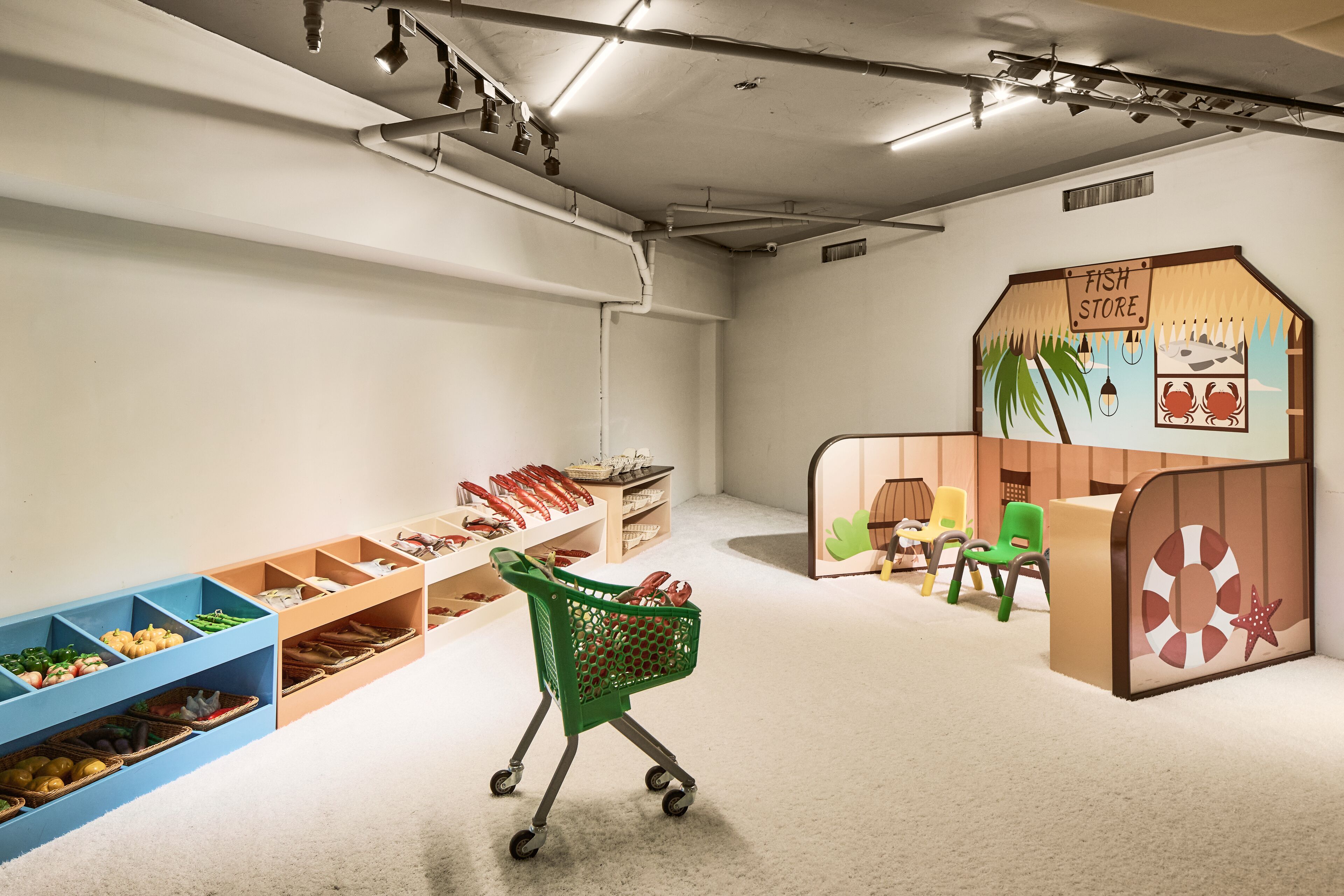 Zona de juegos con temática de tienda de peces, que incluye estantes con juguetes y un carrito de compras.