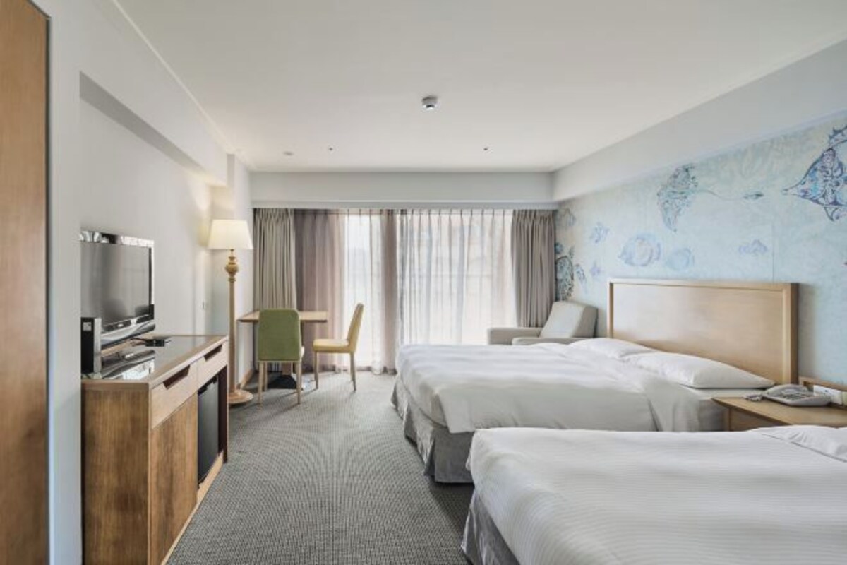 Een hotelkamer met twee bedden, een bureau met een televisie, een stoel en een kaart aan de muur.
