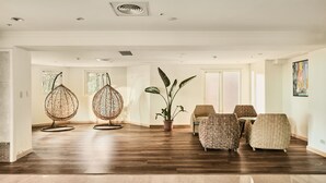 A spacious room with a wooden floor, a large potted plant, and several wicker chairs.