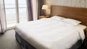 A hotel room with a large bed, a nightstand with a lamp, and a view through a window with curtains.