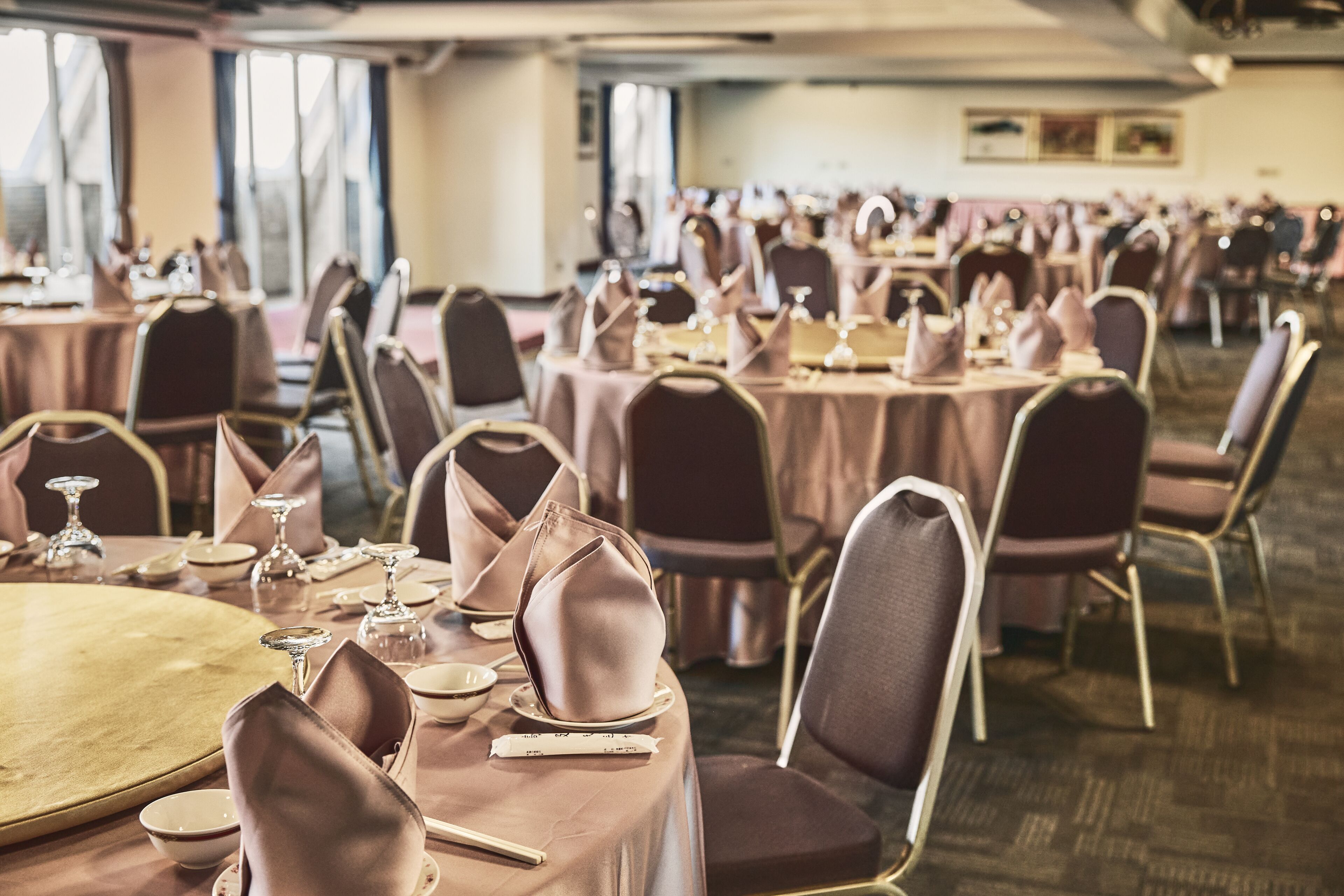 A banquet hall with round tables set for dining, each with a place setting and a folded napkin.