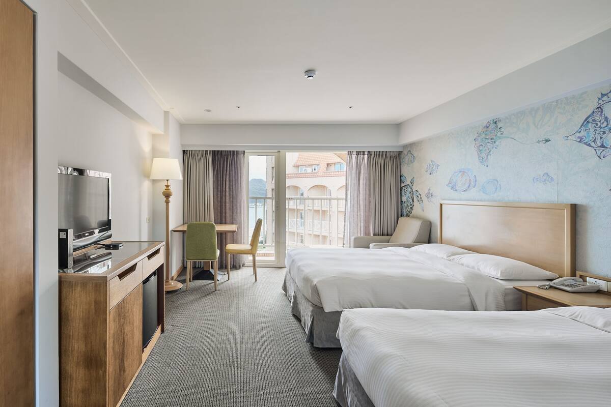 Une chambre d’hôtel avec deux lits, un bureau avec une télévision, une chaise et une vue sur l’extérieur.