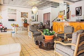 A hotel lobby with a tiled floor, patterned chairs, a central table with a potted plant, and a reception desk. - OYO Historic Cameron Hotel Brownsville I-69E (Brownsville)