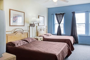 A hotel room with two beds, a nightstand, a lamp, and a window with curtains. - OYO Historic Cameron Hotel Brownsville I-69E (Brownsville)