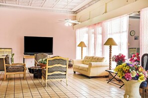 A living room with a television, two lamps, a sofa, a chair, and a floral arrangement. - OYO Historic Cameron Hotel Brownsville I-69E (Brownsville)
