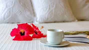Una cama con ropa blanca, una taza de té y un libro sobre una mesa.