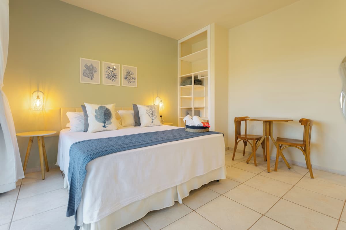 A bedroom with a bed, bedside tables, a chair, a small table, and a shelf unit.