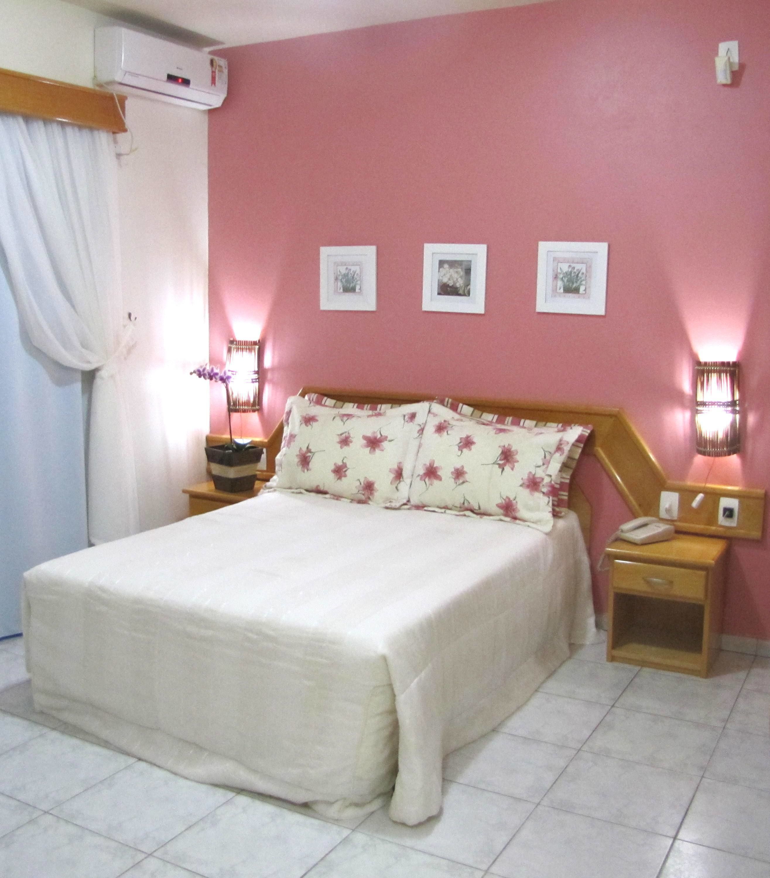 Une chambre à coucher comprenant un lit, des tables de chevet, une commode, un climatiseur fixé au mur et des tableaux encadrés accrochés au mur.