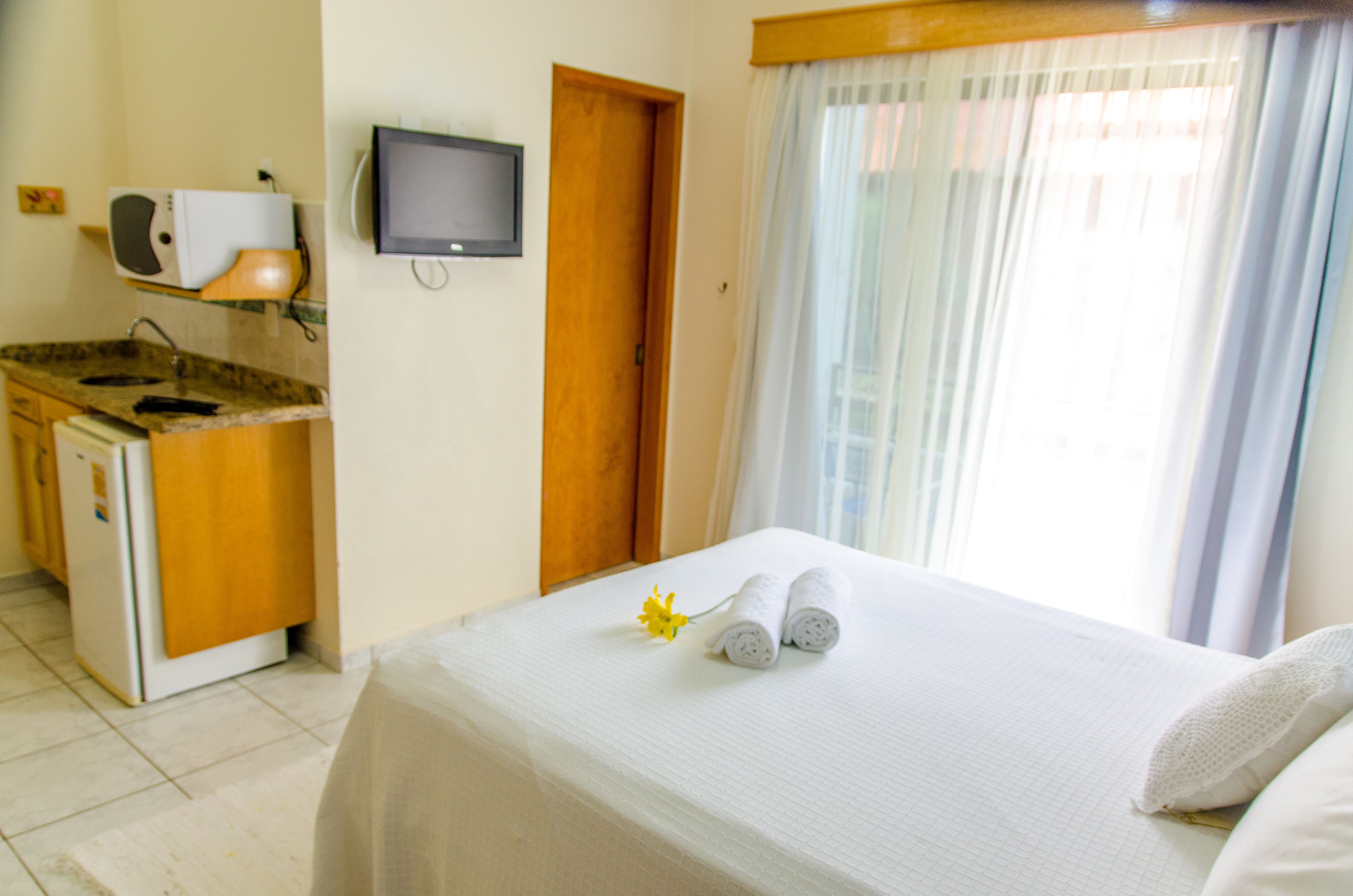 Una habitación de hotel con cama, televisión, una kitchenette pequeña y ventana con cortinas.