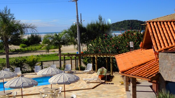 Un espace aménagé au bord de la piscine, avec des chaises longues et des parasols, une terrasse carrelée et une vue sur la plage et l’océan.