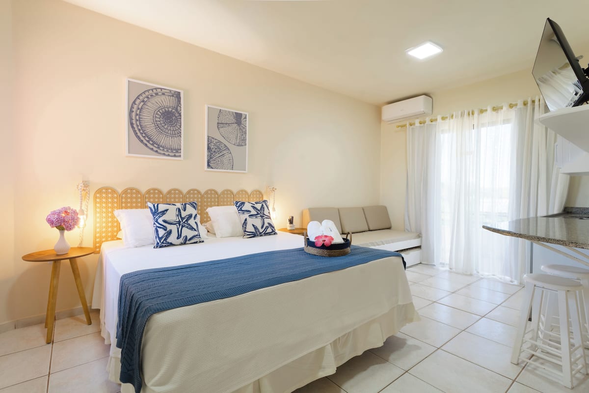 A hotel room with a bed, a small table, a chair, a TV, and a window with curtains.