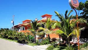 Un bâtiment à deux étages, doté d’une façade rouge et orange, entouré d’une végétation luxuriante et de palmiers.