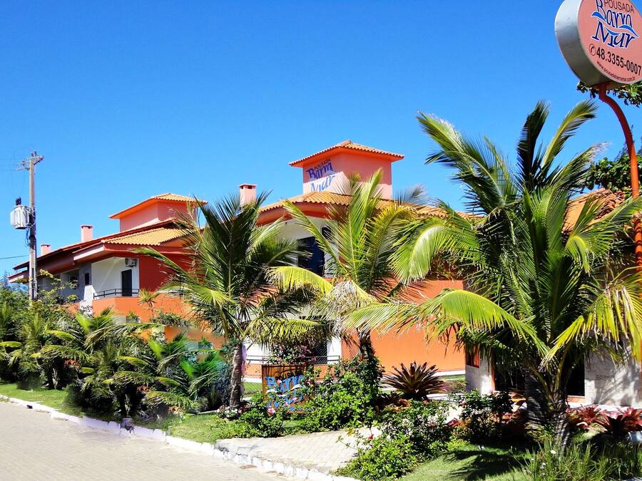 Un edificio de dos plantas con fachada roja y naranja, rodeado de abundante vegetación y palmeras.