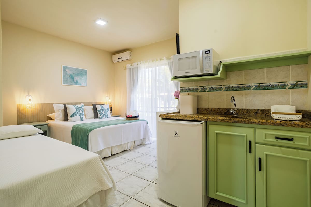 A hotel room with a bed, a small kitchenette, a microwave, a refrigerator, and a window with curtains.