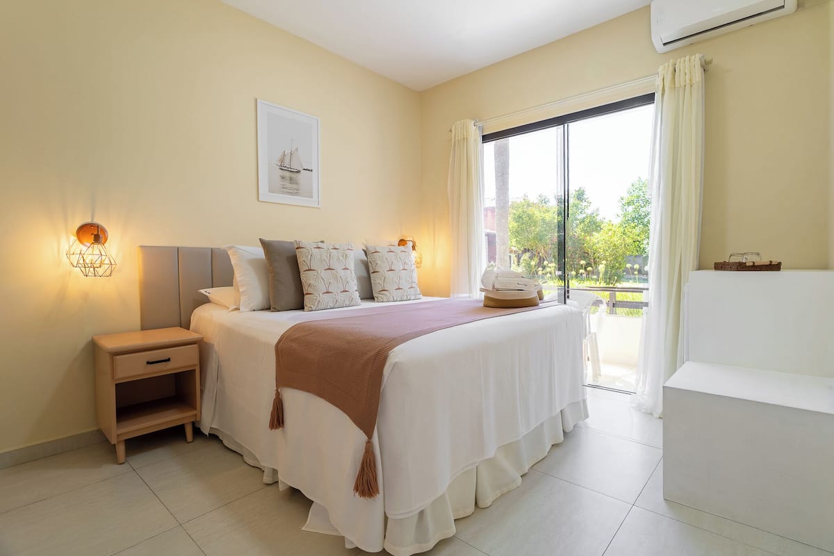 A bedroom with a bed, bedside table, nightstand, and a window with curtains.