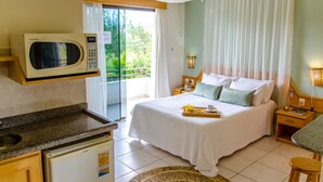 Une chambre d’hôtel comprenant un lit, un four à micro-ondes, un petit réfrigérateur, un balcon avec vue sur la verdure et un coin repas.