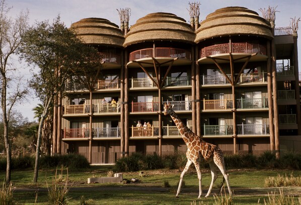 A giraffe walking in front of a building with multiple balconies and a unique architectural design. - Disney's Animal Kingdom Villas - Jambo House (Kissimmee)