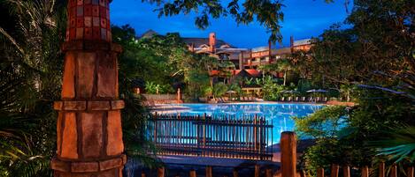 A pool area with a wooden fence, surrounded by lush greenery and a stone pillar.