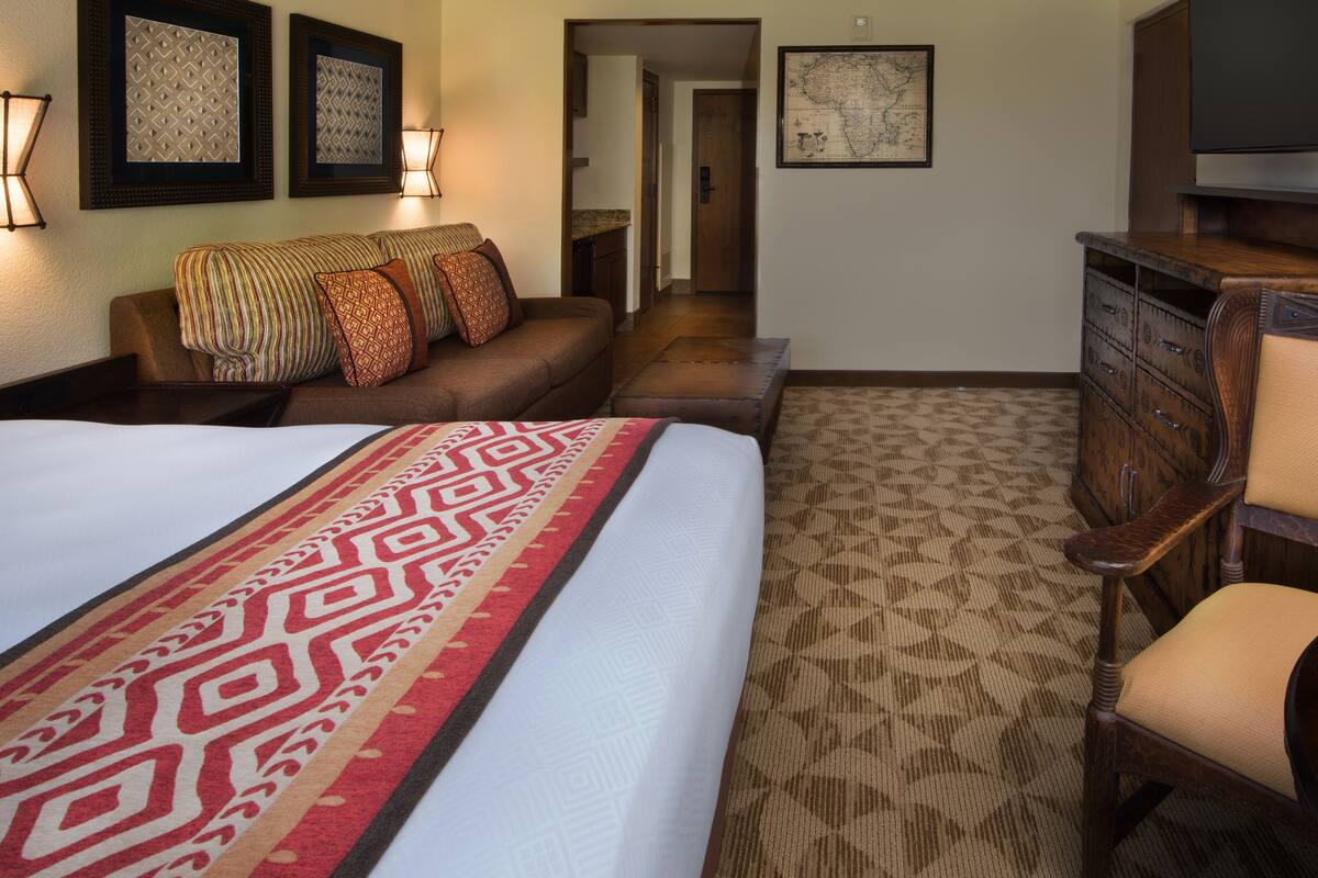 A hotel room with a large bed, a wooden dresser, a television, and a map on the wall.