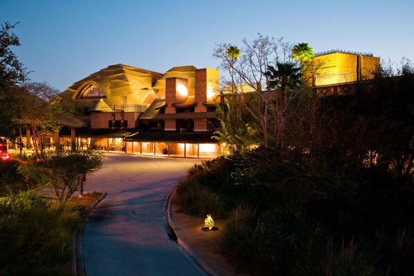 A large, uniquely designed building with multiple levels and a curved roof, surrounded by greenery and a paved pathway leading to the entrance. - Disney's Animal Kingdom Villas - Jambo House (Kissimmee)