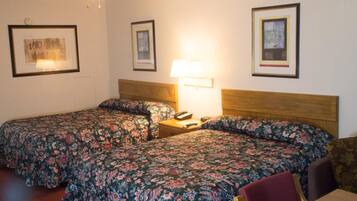 A hotel room with two single beds, a wooden headboard, a bedside table with a lamp, and framed pictures on the walls.