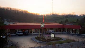 Um motel com telhado vermelho, um letreiro com a inscrição 'TAZEWELL MOTOR LODGE' e um estacionamento com vários carros.