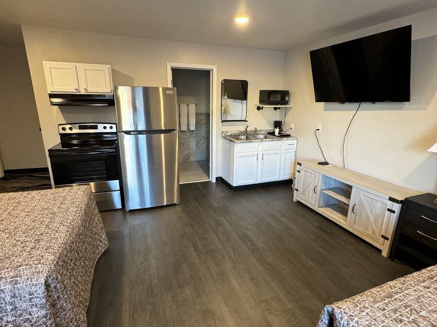 A modern kitchen with stainless steel appliances, a flat-screen TV mounted above the counter, and a separate dining area with a wooden table and chairs.