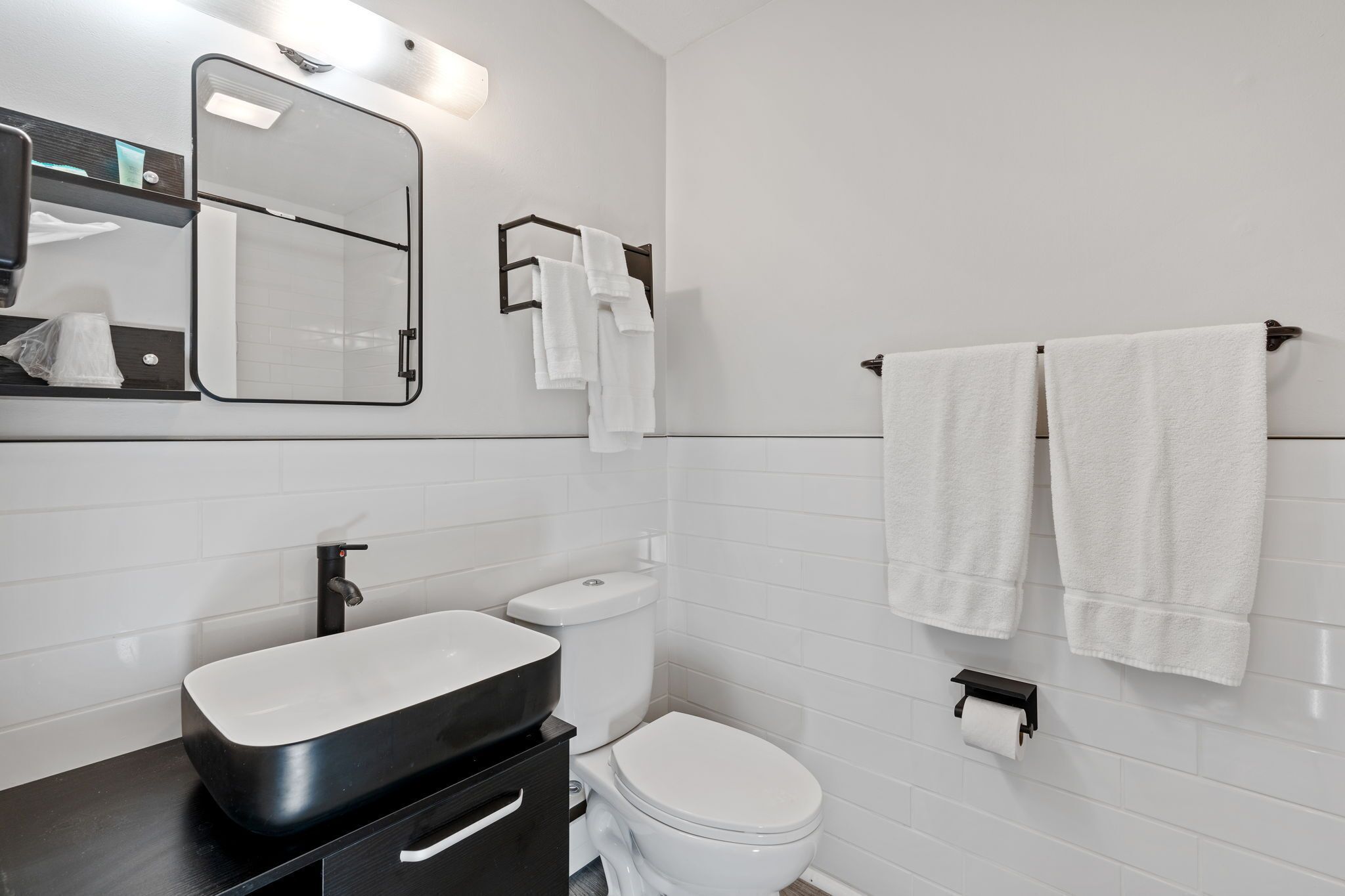 Une salle de bain moderne avec un meuble-lavabo noir, des carreaux blancs, des toilettes et deux serviettes suspendues à un porte-serviettes.