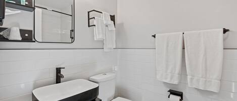 Une salle de bain moderne avec un meuble-lavabo noir, des carreaux blancs, des toilettes et deux serviettes suspendues à un porte-serviettes.