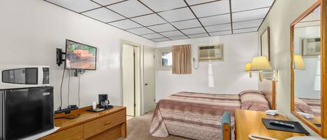 A hotel room with a kitchenette, a bed, a desk with a telephone, and a television.