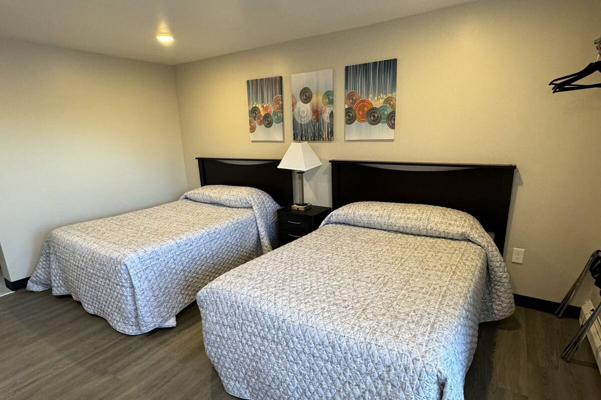 Habitación de hotel con dos camas, una mesita de noche, una lámpara y tres obras de arte en la pared.
