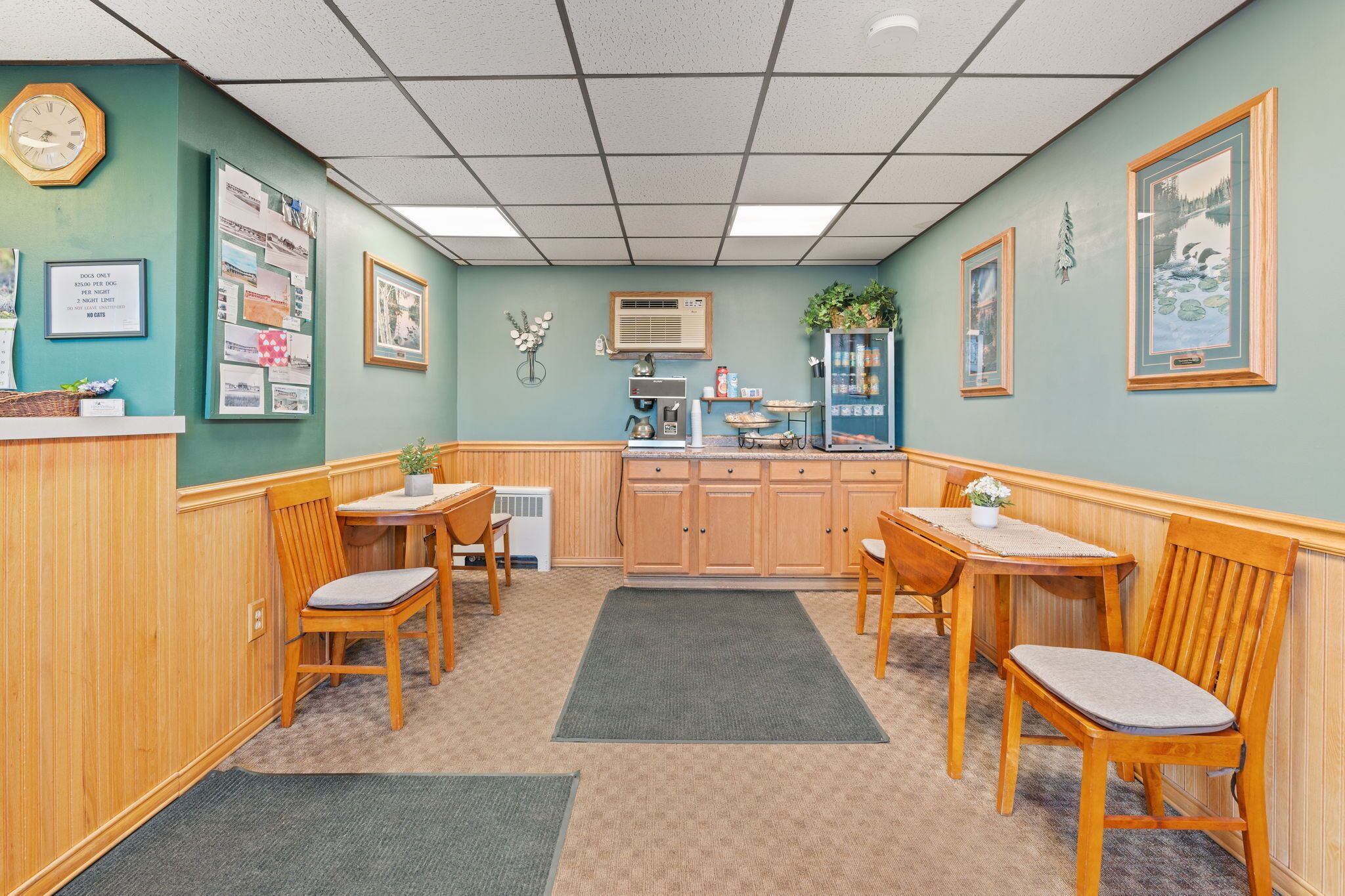 A cozy room with a wooden reception desk, two wooden tables with chairs, a microwave, and a refrigerator.