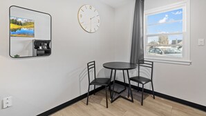 A room with a round table, two chairs, a wall clock, a window with a view of cars, and a mirror reflecting a landscape. - Pine View Inn (Virginia)