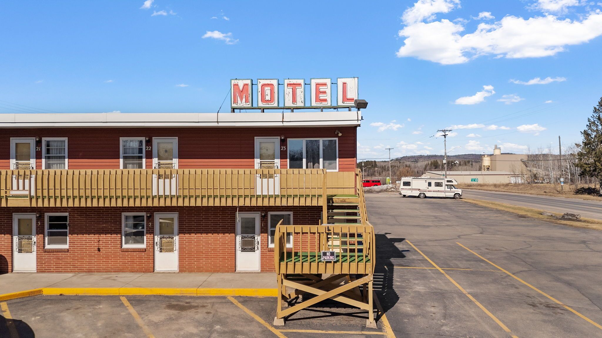 Un motel con facciata rossa, un cartello con la scritta 'MOTEL' in lettere rosse e un'area di parcheggio recintata.