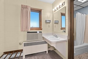 A compact bathroom with a white sink, a mirror, a window with curtains, a heater, and a shower area.