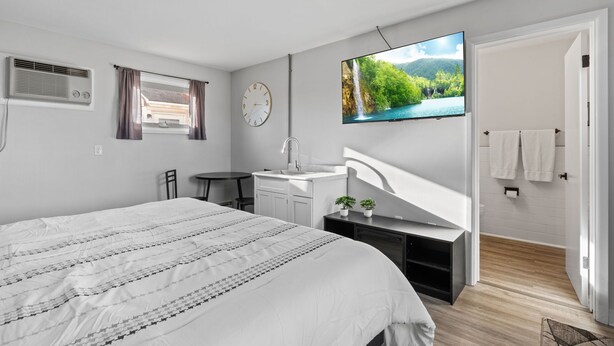 A modern bedroom with a large bed, a desk, a TV, and a bathroom with a shower. - Pine View Inn (Virginia)