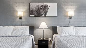 Una habitación de hotel con dos camas, una mesita de noche, una lámpara y un cuadro en la pared.