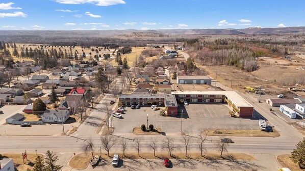 A small town with residential houses, a central building with a parking lot, and a backdrop of hills and trees.