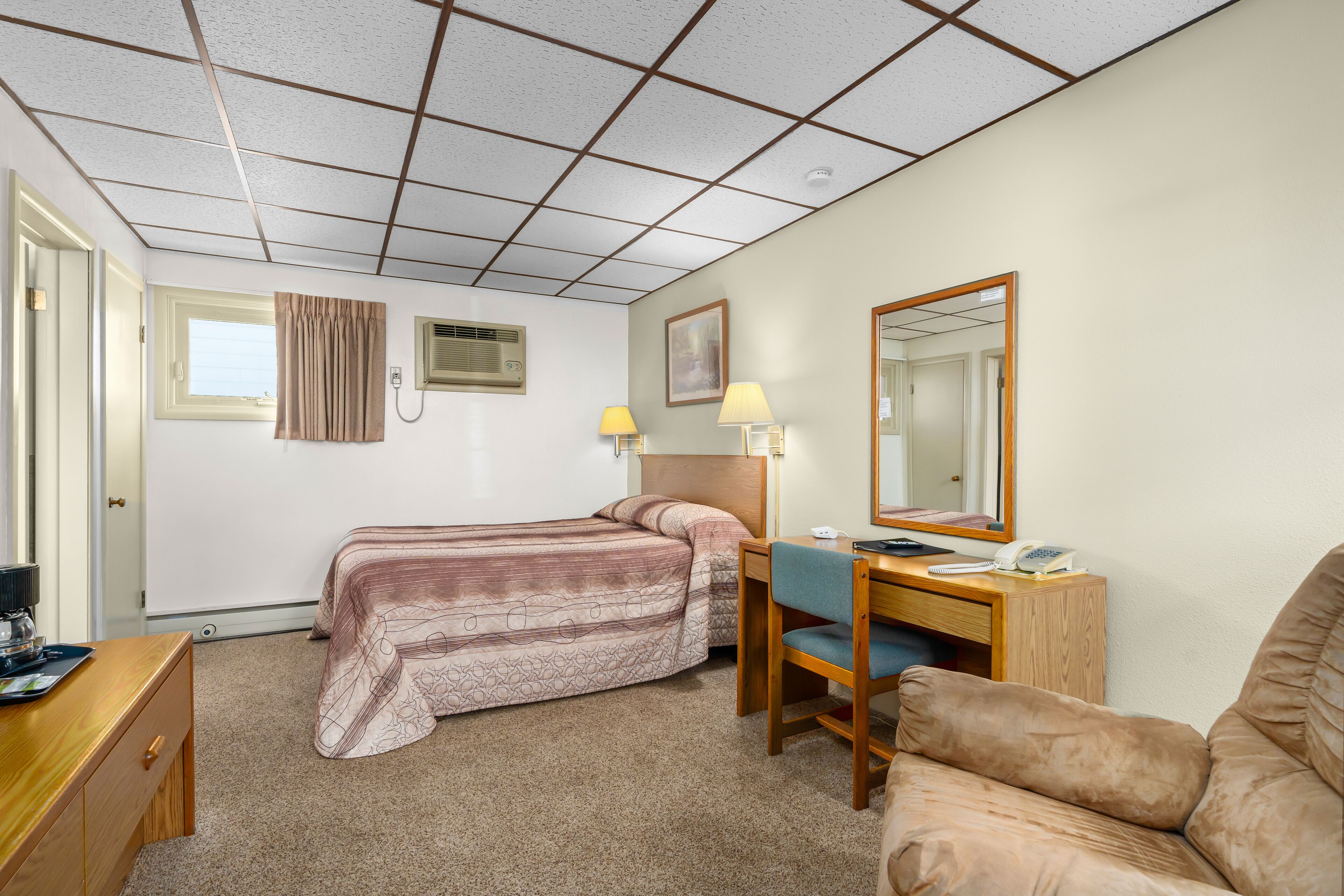 A hotel room with two beds, a desk with a chair, a mirror, and a window.