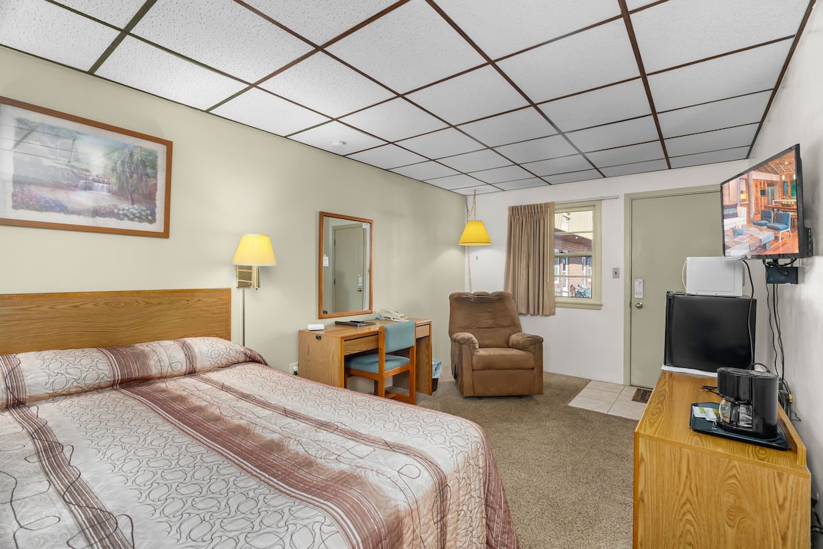Una habitación de hotel con una cama grande, un escritorio con silla, televisión y ventana con cortinas.