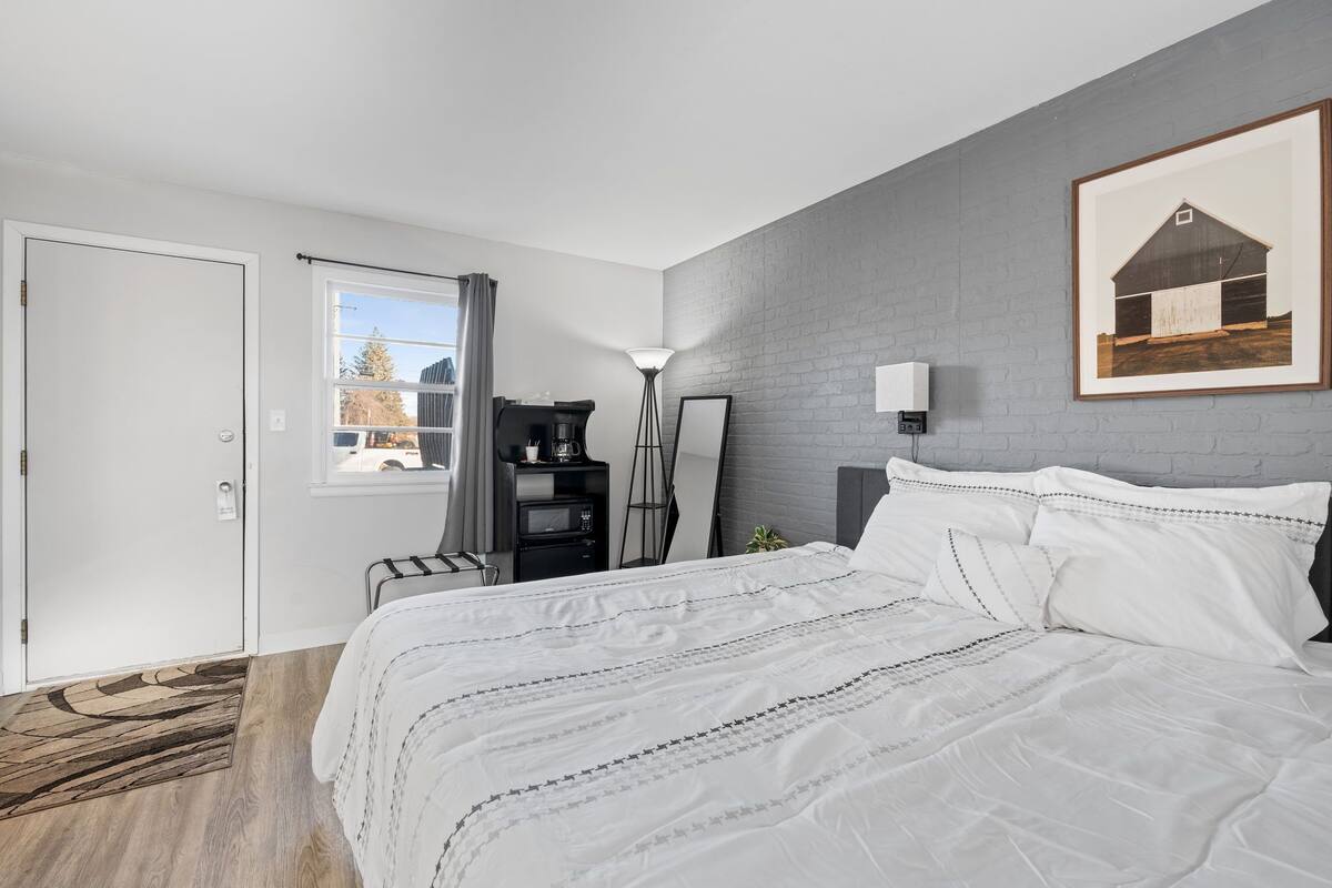 Un dormitorio con una cama grande, un escritorio, una silla, una lámpara y un cuadro en la pared.