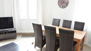 A dining area with a wooden table and six chairs, a television on a stand, and a clock on the wall. - Amazing Apartment Antwerp South (Antwerp)